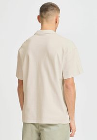 Chemise beige à manches courtes avec un col pointu et une coupe décontractée. Tissu lisse et léger avec des fentes sur les côtés près de l'ourlet.