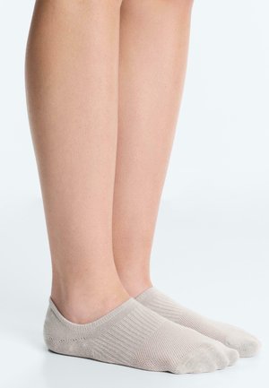 Picioare inferioare purtând șosete invizibile bej deschis, stând pe o suprafață albă netedă, cu un fundal simplu și deschis.