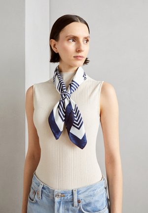 Silk scarf in navy blue and white with a geometric zigzag pattern. Smooth texture, tied neatly around the neck, complementing a ribbed top.