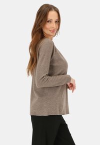 Brązowy sweter z długim rękawem i okrągłym dekoltem, wykonany z miękkiego materiału, o luźnym kroju i subtelnej fakturze. W połączeniu z czarnymi spodniami.