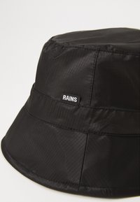 Sort bucket hat lavet af vandafvisende stof, med en tekstureret overflade og et hvidt "RAINS" logo tag på siden.