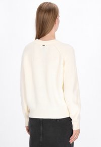 Crème geribbelde gebreide trui met lange mouwen, ronde hals en een zoom die op de taille zit. Bevat een klein logotag aan de achterkant.