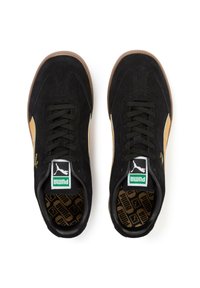 Zapatillas de ante negras con acentos dorados y suela de goma marrón. Presenta cordones negros y un destacado logotipo de Puma en la lengüeta y en la plantilla.