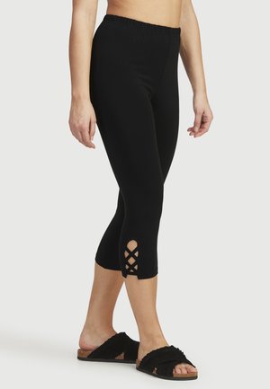 Svarta capri-leggingar med en samlad midja, som har kryssade utskärningar vid fållen. Slät, elastisk tyg och åtsittande design.