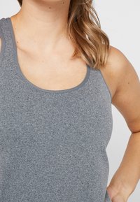 Grå atletisk linne med rundad halsringning, tillverkat av ett texturerat tyg. Har smala axelband och en åtsittande silhuett. Inga märkbara mönster.