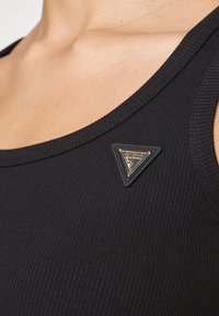 Must värviline triibuline särk, millel on vasakul küljel kolmnurkne kuldne ja must logo, näidates sujuvat kangast ja lähedalt istuvat lõiget.
