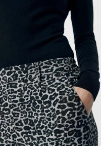 Zwarte lange mouw top gecombineerd met grijze broek met een zwart luipaardpatroon. De broek heeft een zak en zichtbare stikseldetails.