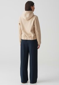 Hoodie cropped beige con cordini e orlo a costine, abbinato a pantaloni a gamba larga blu navy. Texture del tessuto liscia e design minimal.