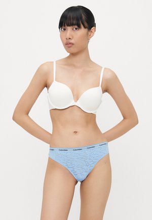 Bijeli grudnjak s oblikovanim cups i tankim trakama; plavi čipkani thong s Calvin Klein logotipom na pojasu; glatke teksture i prilagođen dizajn.