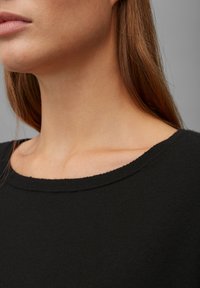 Schwarzer Strickpullover mit weitem, runden Ausschnitt. Glatte Textur und weicher Stoff. Nahaufnahme des Schulter- und Kragenbereichs.