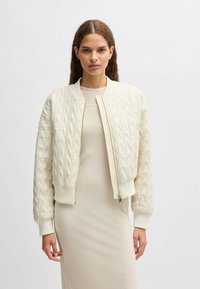 Quilted cream bomber jacket with ribbed cuffs and hem, featuring a front zip closure and a smooth, satin-like texture.