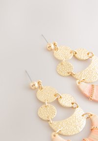 Gold-tone earrings featuring textured circular and crescent shapes with a blend of smooth and hammered finishes. Includes a pink textile accent.