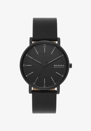 Schwarze minimalistische Armbanduhr mit Lederarmband, rundem Zifferblatt, weißen Markierungen, drei Zeigern und "Skagen Denmark" Branding auf dem Zifferblatt.
