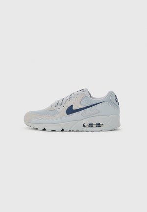 Jasnoszary sneaker Nike Air Max z ciemnoniebieskim logo Swoosh i widoczną podeszwą z amortyzacją powietrzną, widok z boku na jednolitym tle.