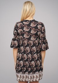 Musta mekko, jossa on punavalkoinen paisley-kuvio, kerrokselliset volangihihat ja kerroksellinen hame. Liukas kangas.
