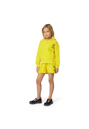 Sweat à capuche en éponge jaune avec zip, featuring un motif de tournesol. Associé à une jupe assortie et des chaussures navy avec des accents rouges.