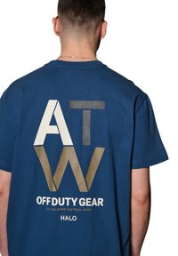 Blauwe katoen t-shirt met groot grafisch tekst "ATW" in wit, zwart en goud op de achterkant, met daaronder "OFF DUTY GEAR" en de merknaam.