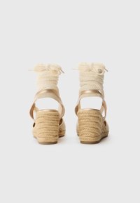 Espadrille kilklackar med en flätad jutehæl, krämfärgade tygremmar och ett strukturerat ankelsnöre, med en gyllene detalj på sidorna.