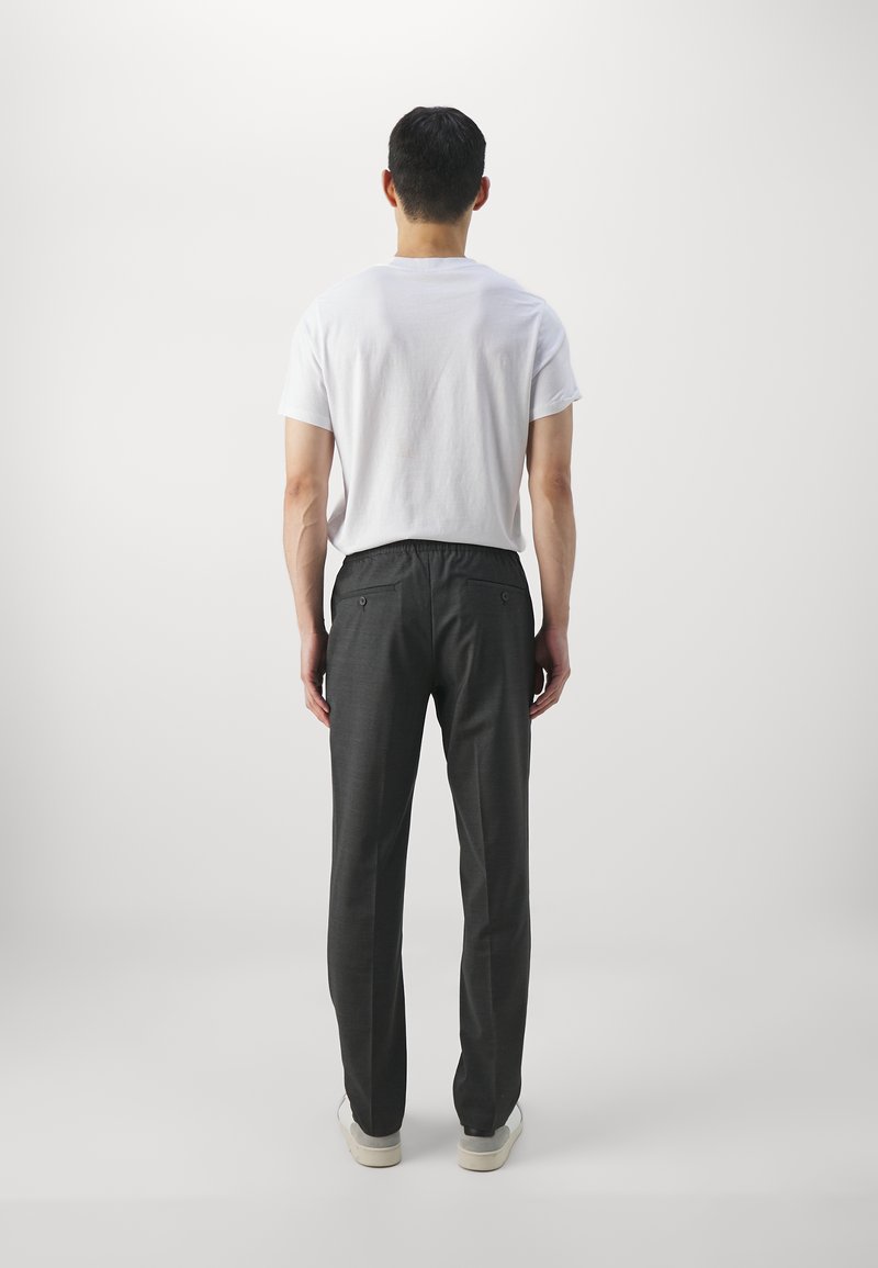 Graue Hose mit entspannter Passform, elastischem Bund und Gesäßtaschen, kombiniert mit einem schlichten weißen T-Shirt und lässigen Turnschuhen.