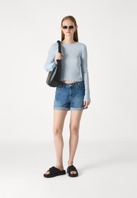 Maglietta a maniche lunghe rigata blu chiaro, pantaloni corti in denim, borsa nera a tracolla e sandali neri scivolati. Outfit semplice e casual con una vestibilità rilassata.