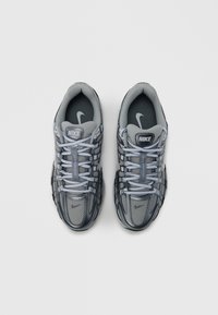 Τα γκρι αθλητικά παπούτσια Nike διαθέτουν υλικά από δίχτυ και συνθετικά, με πουά μοτίβο, αντίθετες μαύρες σόλες και ανοιχτό μπλε κορδόνια.