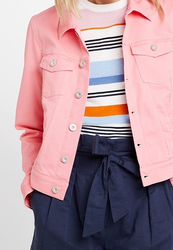 Chaqueta de mezclilla rosa con botones plateados, dos bolsillos en el pecho y cuello puntiagudo, combinada con un suéter a rayas y pantalones de tiro alto en color navy.