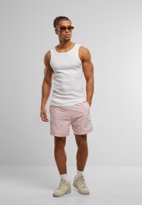 Hvit tank topp og lyse rosa shorts med logo, beige sneakers og solbriller. Teksturen ser jevn ut, og passformen er atletisk.