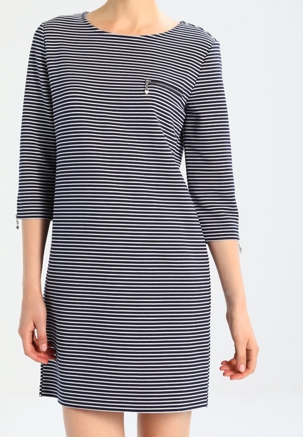 Femme portant une robe à rayures horizontales bleu marine et blanche, avec des manches trois-quarts et une petite poche zippée sur la poitrine.