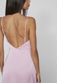 Rosa satin klänning med låg V-ryg, justerbara tunna axelband och slät textur, som flödar ner till en knälång fåll.