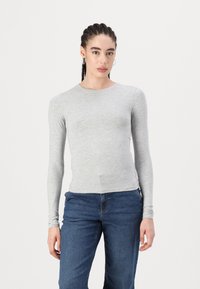 Haut à manches longues gris en tissu doux, avec un col rond et une coupe ajustée, associé à un jean bleu pour un look décontracté.