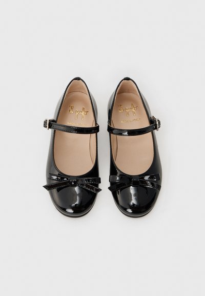 Chaussures Mary Jane en cuir verni noir avec un bout ronde, une bride à boucle et un nœud décoratif à l'avant. Texture lisse.