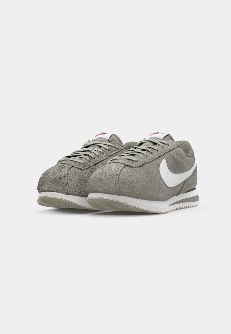 Scarpe sportive in suede grigio con accenti bianchi, tomaia texturizzata e suola in gomma bianca con battistrada a zigzag. Design con lacci e cuciture visibili.