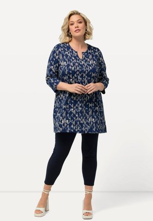Marineblaues Oberteil mit geometrischem cremefarbenem Muster, dreiviertel Ärmel, runder Ausschnitt, kombiniert mit marineblauen Leggings und weißen Plateauschuhen.