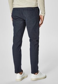 Dark blue slim-fit trousers, woven fabric, two back pockets, paired with white sneakers, featuring a minimalist design and no visible patterns.