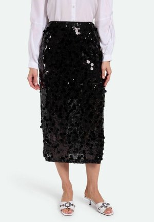 Schwarzer Pailletten-Midirock mit figurbetontem Schnitt, der kreisförmige Pailletten für Textur aufweist. Getragen mit einer weißen Bluse mit langen Ärmeln und weißen High Heels.