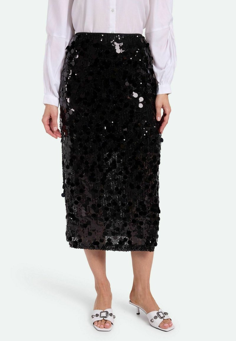 Falda midi de lentejuelas negras con una silueta ajustada, que presenta lentejuelas circulares para dar textura. Combinada con una blusa blanca de mangas largas y tacones blancos.