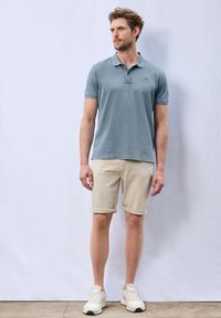 Ljusblå bomulls polo skjorta, beige uppvikta shorts och vita sneakers. Enkelt design med korta ärmar och krage.
