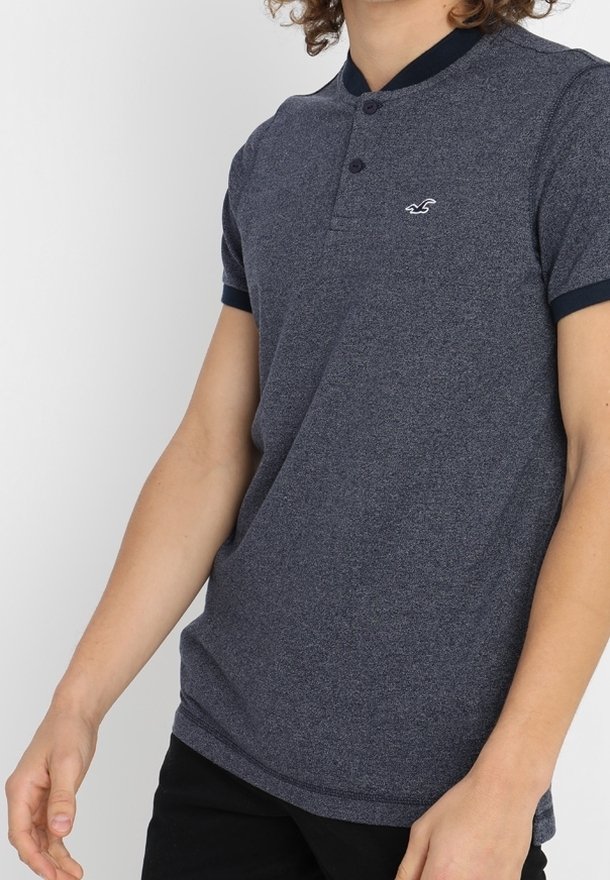Marinblå polo skjorta med korta ärmar, texturerad tyg och två-knappsstängning. Har en liten logo på bröstet och kontrasterande krage.