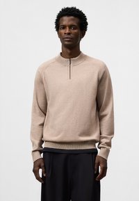 Maglione beige a maglia con colletto a mezza zip e polsini a costine. Presenta una vestibilità rilassata e una texture fine, abbinato a pantaloni scuri.