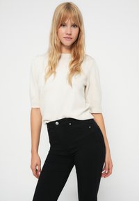 Light cream short-sleeve sweater with a round neckline, paired with high-waisted black jeans featuring silver hardware and a fitted design.