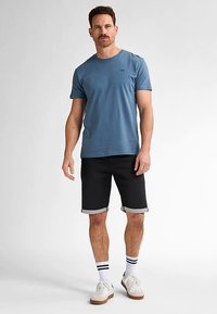 Blauw katoenen T-shirt met ronde hals, gecombineerd met zwarte spijkershorts met omgeslagen zoom, witte sokken met zwarte strepen en witte sneakers.