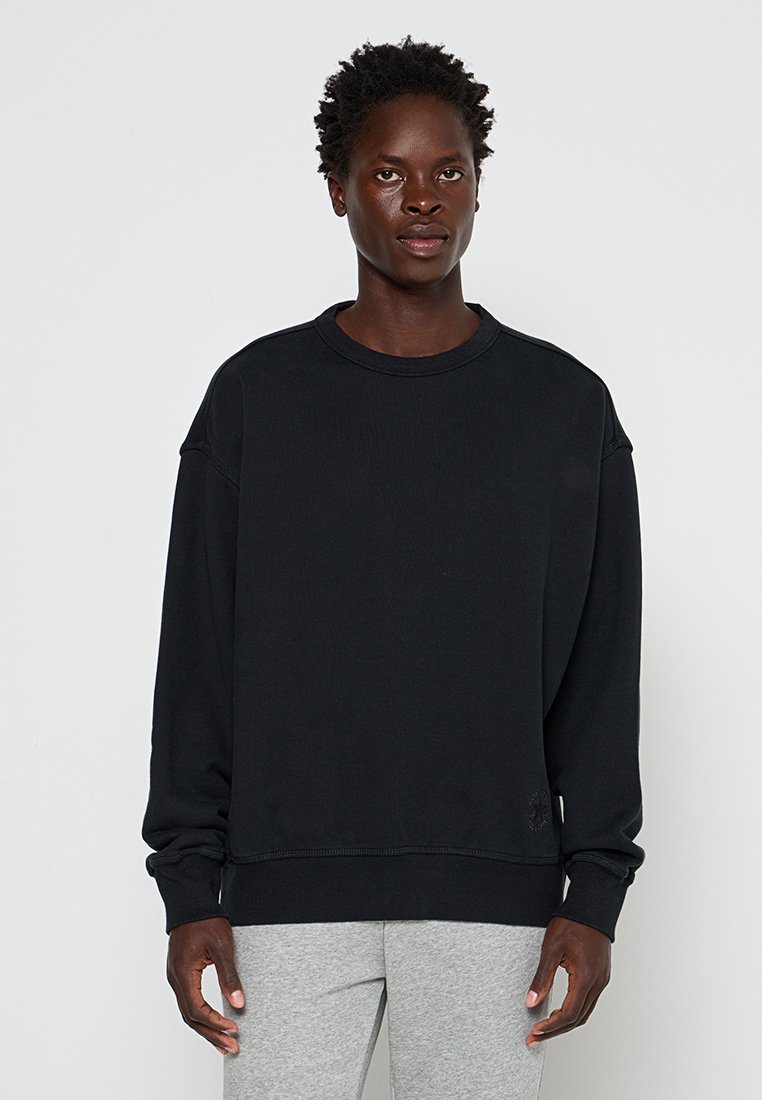Felpa nera a collo rotondo con maniche lunghe, realizzata in tessuto testurizzato. Presenta polsini e orlo a costine, con un piccolo dettaglio del logo sulla parte anteriore.