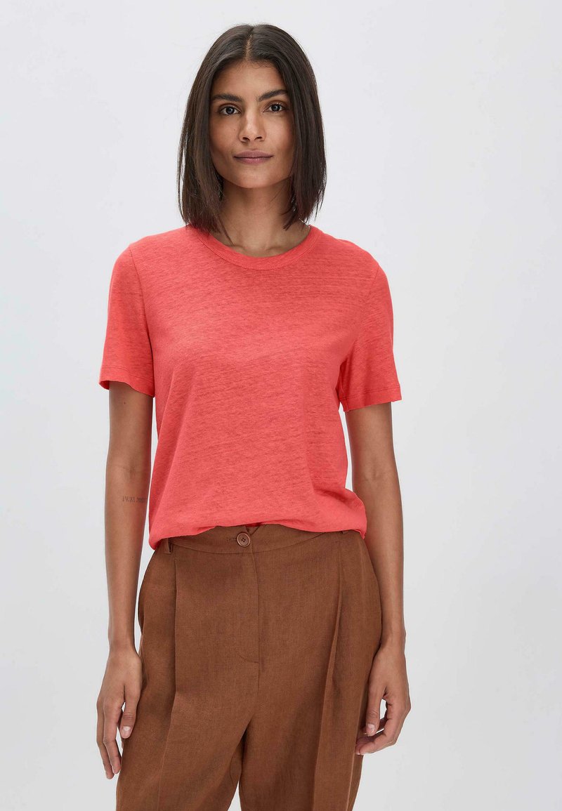 Korallinvärinen lyhythihainen T-paita, jossa on pyöreä pääntie, valmistettu kevyestä materiaalista. Yhdistetty ruskeisiin korkeavyötäröisiin pellavahousuihin, joissa on nappidetali.