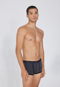 Bóxer de algodón negro con un diseño ajustado, que presenta una cinturilla en contraste etiquetada "TEZENIS" y una textura suave.