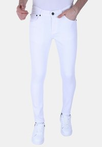 Witte skinny jeans van denim met een aansluitend ontwerp, vijf zakken, knoopsluiting en zwarte accenten op de klinknagels. Gecombineerd met witte sneakers.