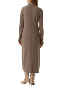 Langes, eng anliegendes Strickkleid in sanftem Braun. Verfügt über gerippte Bündchen und einen Kragen, eine zentrale Nahtdetail und reicht bis zur Mitte der Waden. Getragen mit beigen Ankle-Boots.