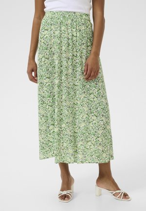 Floral maxi-jurk met een smockelastische tailleband. Lichtgroene stof met kleine, meerkleurige bloemen. Model draagt witte hakkensandalen.
