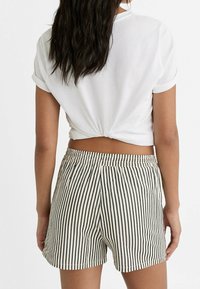 Biały, krótki top z krótkim rękawem, wiązany z tyłu; w zestawie beżowo-granatowe szorty w paski z elastycznym paskiem w talii i bocznymi kieszeniami.