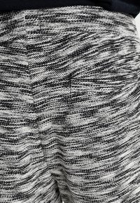 Gros plan sur un pantalon en tissu texturé noir et blanc avec une poche latérale dissimulée et un motif de tissage horizontal fin.