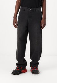 Black denim jeans with a loose fit, featuring a standard waistband, front pockets, and a solid texture. Paired with black and red sneakers.
